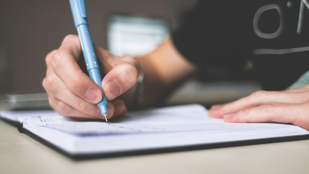 a person is holding a pen and writing in a notebook